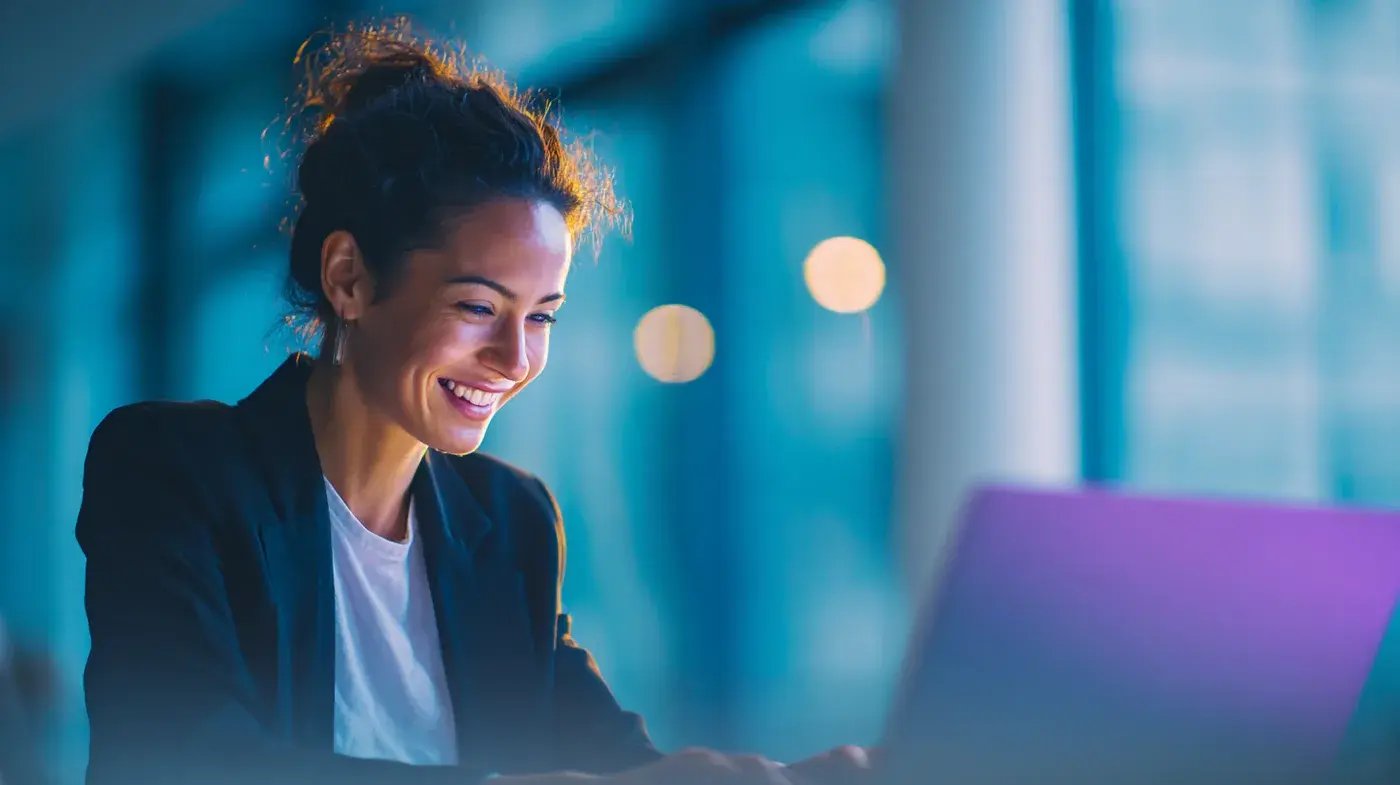 Une professionnelle sourit devant son ordinateur portable, dans un bureau aux tons bleus