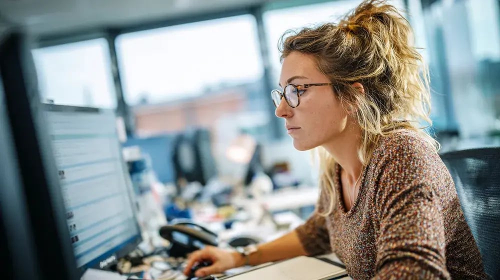 Une professionnelle à lunettes travaille sur son ordinateur dans un bureau lumineux